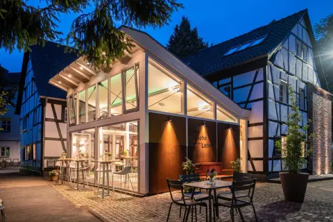 Abendstimmung an der buchmühle bergisch gladbach. Moderne Glasfront trifft auf Fachwerkhaus. Tische und Stühle laden zum Verweilen ein.