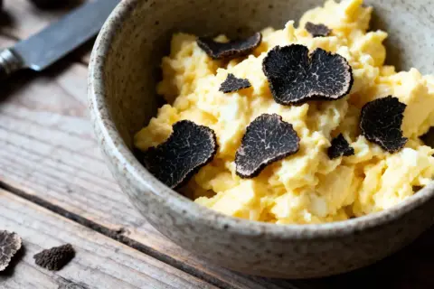 Œufs brouillés garnis de fines lamelles de variétés de truffes noires. Un délice sur fond de bois rustique.