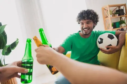 Un homme souriant avec un ballon de foot trinque avec des bières, une récompense parfaite après le sport.