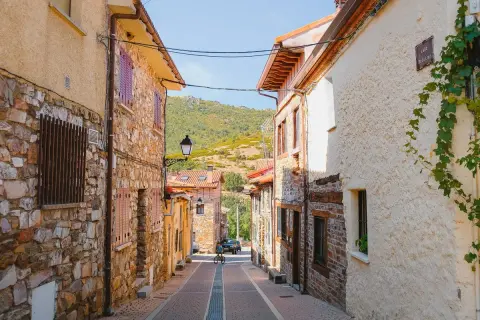 Calle empedrada en Puebla de la Sierra que ver. Casas de piedra y tejados rojos, con colinas verdes al fondo.