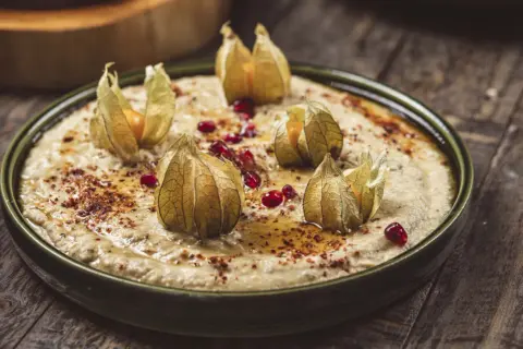 Krämig baba ganoush toppad med physalis och granatäppelkärnor på en rustik träyta.
