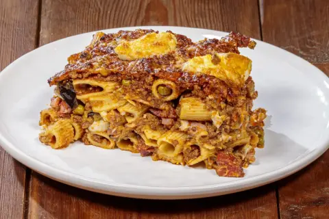 Porzione di pasta ncasciata ricca e saporita, con rigatoni, ragù, uova e verdure, servita su un piatto bianco.