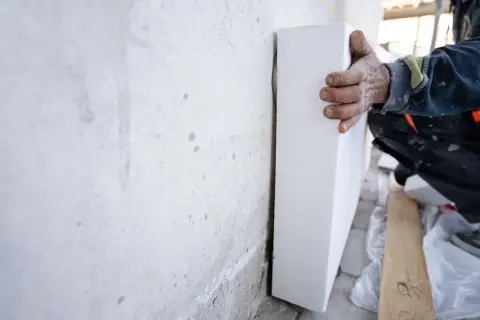 Mano posiziona pannello bianco, uno dei tanti materiali isolanti, contro un muro grezzo.