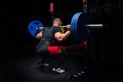 Stark man gör en tung knäböj med skivstång, redo för sitt madcow 5x5 pass.