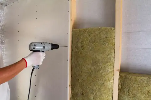 Instalación de aislamiento para como aislar una pared del ruido de los vecinos. Se atornilla placa de yeso sobre estructura de madera con lana mineral.