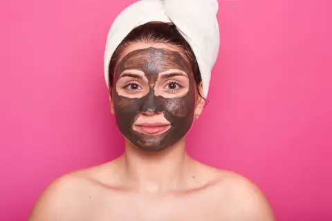 Una mujer con una toalla en la cabeza y una mascarilla de barro en la cara cansada, lista para un tratamiento de spa.