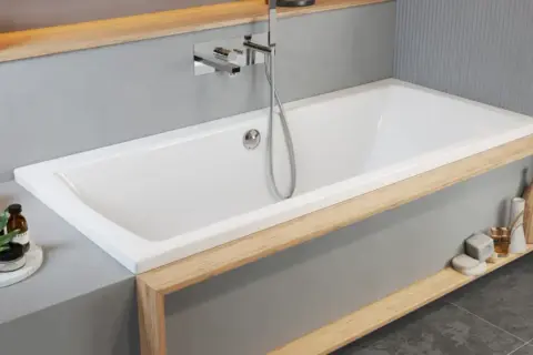 Moderne Badewanne einbauen: Weiße Wanne mit Holzakzenten, Armatur und Handbrause. Dekorative Elemente wie Lampen und Flaschen schmücken die Ablage.