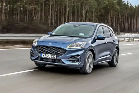 Niebieski Ford Kuga z silnikiem 1.5 Ecoboost pędzi po autostradzie wśród drzew.