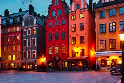 Färgstarka hus i **altstadt Stockholm** lyser upp en kullerstensbelagd gata i skymningen.