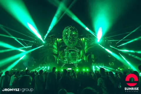 Niesamowita scena z zielonymi światłami i głową z cyframi na Sunrise Festival. Tłum bawi się przy muzyce, czekając na ogłoszenie line-up.