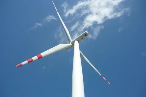 Biała mała elektrownia wiatrowa z czerwonymi pasami na łopatach obraca się na tle błękitnego nieba z chmurami.