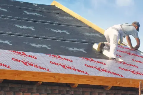 Pracownik montuje ocieplenie nakrokwiowe na dachu, układając warstwy izolacji i membrany.