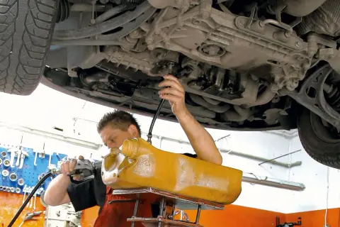 Mechanik wymienia olej w skrzyni biegów DSG, używając żółtego zbiornika i pompy.