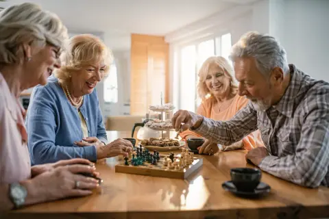 Kto to jest senior? To oni: cztery uśmiechnięte osoby grające w szachy przy kawie i ciastkach.