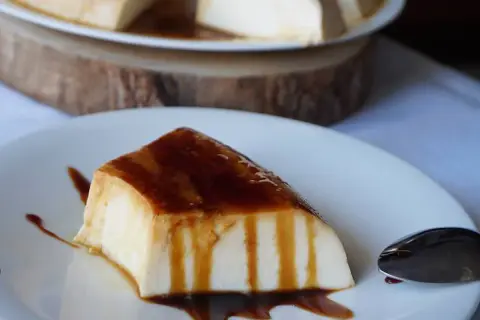 Un trozo de tarta de cuajada, cubierto de caramelo líquido, reposa en un plato blanco.