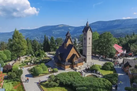 Drewniany kościółek i wieża na tle górskich krajobrazów. Czy to Karpacz, czy Szklarska Poręba?