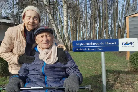 Uśmiechnięta para seniorów pozuje przy tablicy "Alejka Hrabiego de Rosset" w dom seniora Rotmanka.