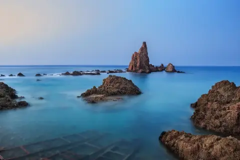 Rocas emergiendo de aguas turquesas en el fondo marino de Cabo de Gata. El cielo se funde con el mar en un amanecer sereno.