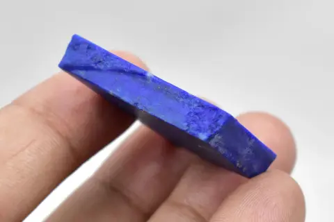 Królewski lapis lazuli, kamień o intensywnym niebieskim kolorze, trzymany w palcach.