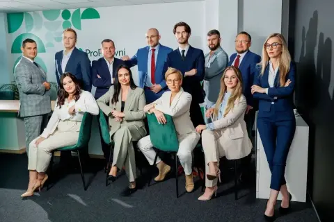 Grupa profesjonalistów w garniturach pozuje do zdjęcia w nowoczesnym biurze.