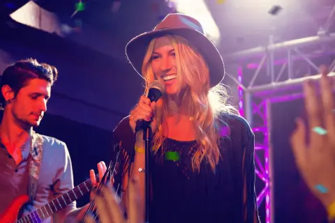 Cantanti marchigiani sul palco, una donna con cappello canta al microfono, un chitarrista suona.