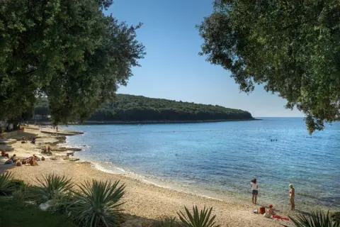Słoneczny dzień na plaży w Porto Sole. Ludzie odpoczywają na kamienistym brzegu, a w krystalicznie czystej wodzie widać kąpiących się.