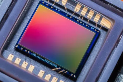 Sensore di immagine 576 megapixel con sfumature arcobaleno, collegato da sottili fili dorati a contatti metallici.