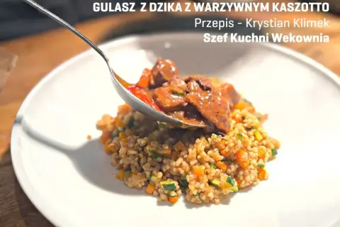 Gulasz z dzika z kaszotto warzywnym. Łyżka nakłada aromatyczne mięso na talerz pełen zdrowego kaszotto.