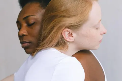 Twee vrouwen, één met donkere huid, de ander met lichte huid, omhelzen elkaar. Een beeld van verbinding, dat het verschil tussen compassie en empathie illustreert.