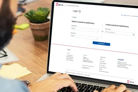 Na ekranie laptopa widzimy stronę logowania do Profilu Zaufanego. Użytkownik szuka swojego Banku Spółdzielczego, aby założyć profil zaufany w Santander.