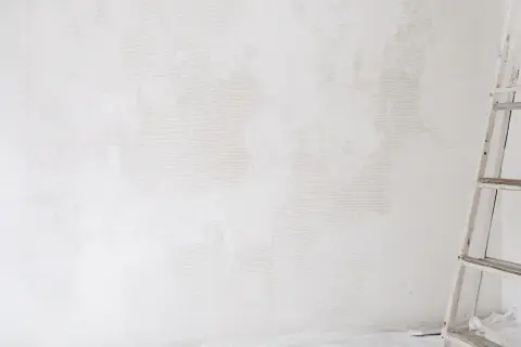Étape de nettoyage d'un mur blanc jauni, une échelle est visible sur la droite.