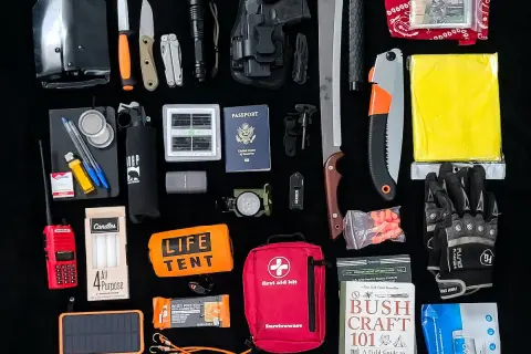 Un conjunto de herramientas EDC para supervivencia: pala plegable, cuchillos, linterna, multiherramienta, pistola, brújula, kit de primeros auxilios, sierra, manta térmica, guantes, libro de supervivencia y más.
