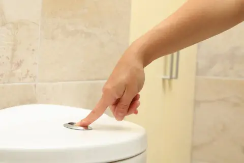 Dłoń naciska przycisk spłuczki. Szukasz domowych sposobów na zbyt częste oddawanie moczu?