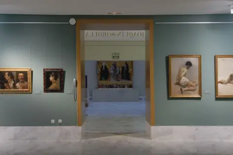 Wnętrze muzeum sztuk pięknych w Walencji. Obrazy wiszą na zielonych ścianach, a marmurowa podłoga odbija światło.