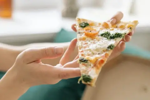 Kawałek pizzy z pomidorkami i szpinakiem, trzymany w dłoniach. Tak jeść pizzę we Włoszech – delektując się każdym kęsem.