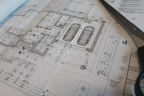 Projekt architektoniczno budowlany domu z garażem, nożyczki przecinają plany.