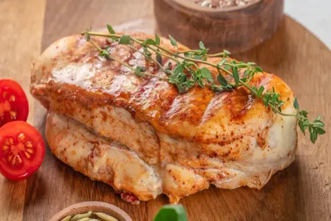 Soczysty filet z indyka duszony, z gałązką tymianku i pomidorkami koktajlowymi na desce.