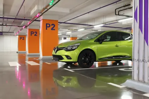 Une voiture verte est garée en bataille dans un parking souterrain, avec des poteaux orange marqués "P2".
