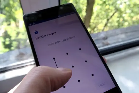 Telefon z ekranem blokady, gdzie wybierasz **wzór** 15 najpopularniejszych blokad. Palec rysuje linię na siatce kropek.