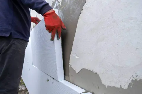 Man con guantes naranjas coloca poliestireno para aislar fachadas.