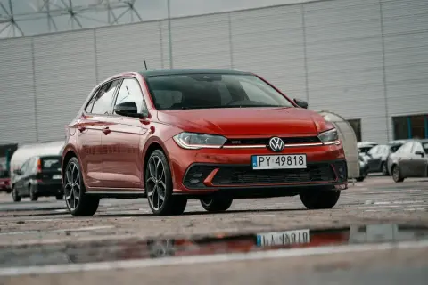 Czerwony Volkswagen Polo GTI z czarnym dachem, zaparkowany na mokrym parkingu.