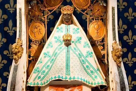 Statue de la Vierge noire couronnée, entourée de symboles religieux. Une image qui raconte une partie de l'histoire de la vierge noire.