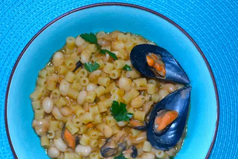 Piatto di pasta fagioli e cozze, un classico della cucina italiana, servito in una ciotola azzurra su un tovagliolo blu.