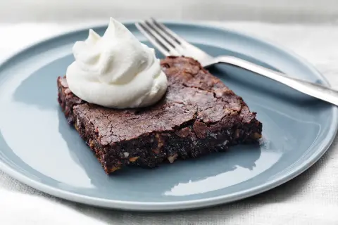En saftig brownie med nötter, toppad med vispad grädde, redo att avnjutas. Perfekt för ett enkelt brownie recept.