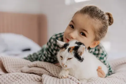 Mała dziewczynka przytula swojego kota. Ich więź jest widoczna, gdy kot wtula się w jej ramiona.