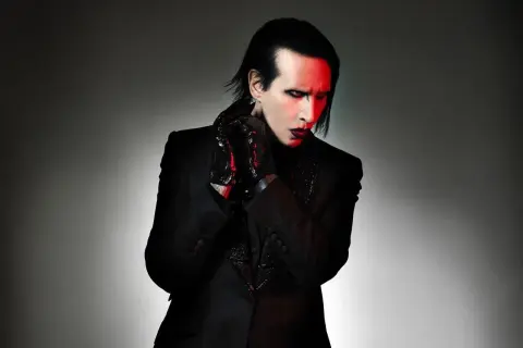 Marilyn Manson zespół w czarnym garniturze, z czerwonym makijażem i rękawiczkami.