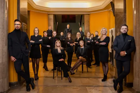 Grupa profesjonalistów w eleganckich strojach pozuje w holu.