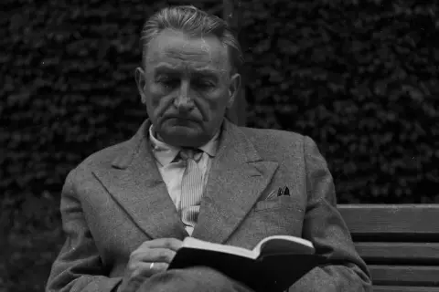 Zamyślony mężczyzna w garniturze czyta książkę na ławce. Może w tej chwili myśli, że życie mnie mnie fraszka, szukając ukojenia w literaturze.