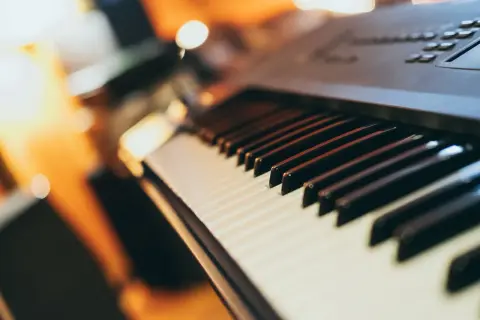 Klawiatura keyboardu, gotowa na naukę gry. Ciepłe światło otoczenia podkreśla czarne i białe klawisze, zapraszając do muzycznej podróży.