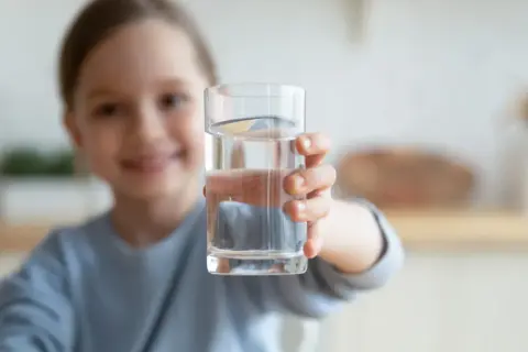 Uśmiechnięta dziewczynka podaje szklankę czystej wody. To doskonały wybór, jaka woda dla rocznego dziecka.